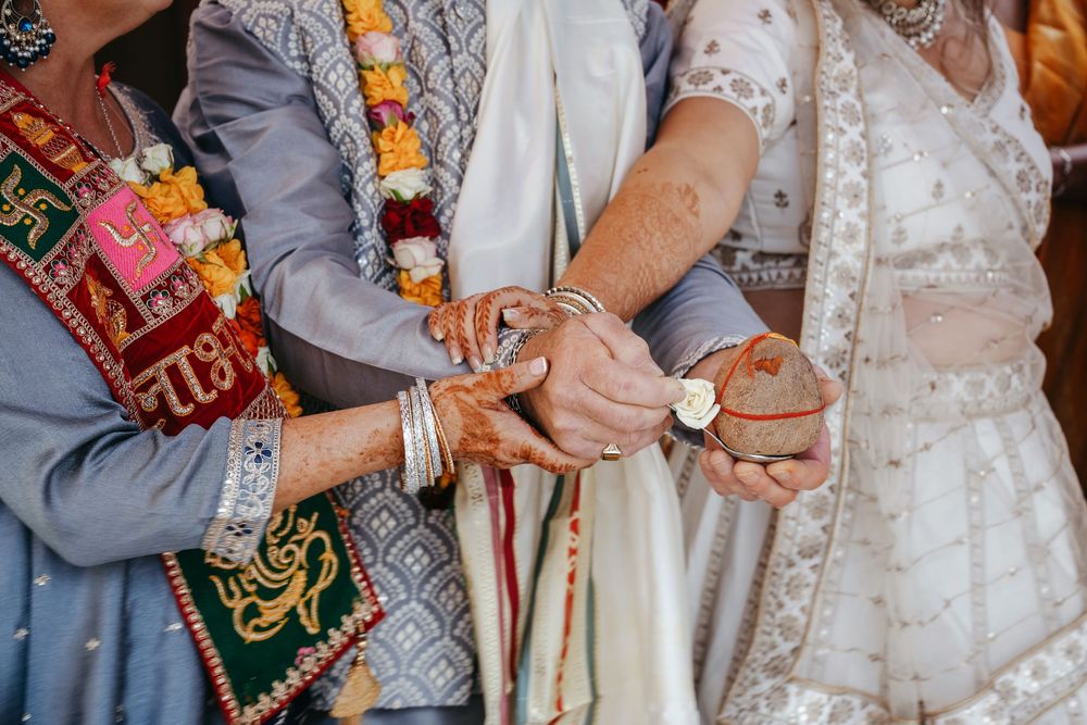 Close-up of hands joined during a traditional Indian wedding ceremony, adorned with mehndi, bangles, and floral garlands.
