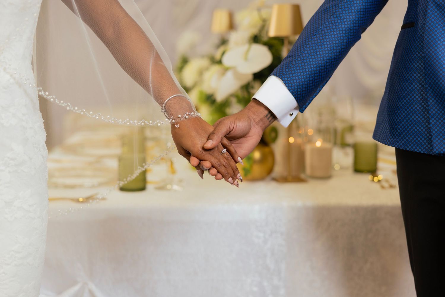 Bride and groom holding hands at wedding altar with floral arrangements and candles in the background.
