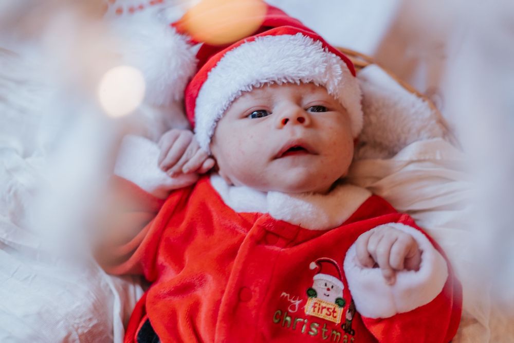 Newborn baby dressed in a red Santa Claus outfit and hat lying down during Christmas holiday celebration.