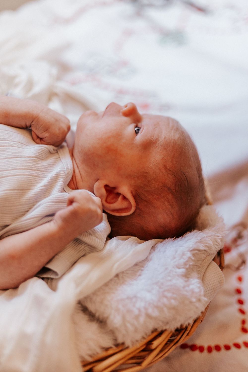 Peaceful newborn baby lying in a wicker basket on a soft white blanket, gazing upward.