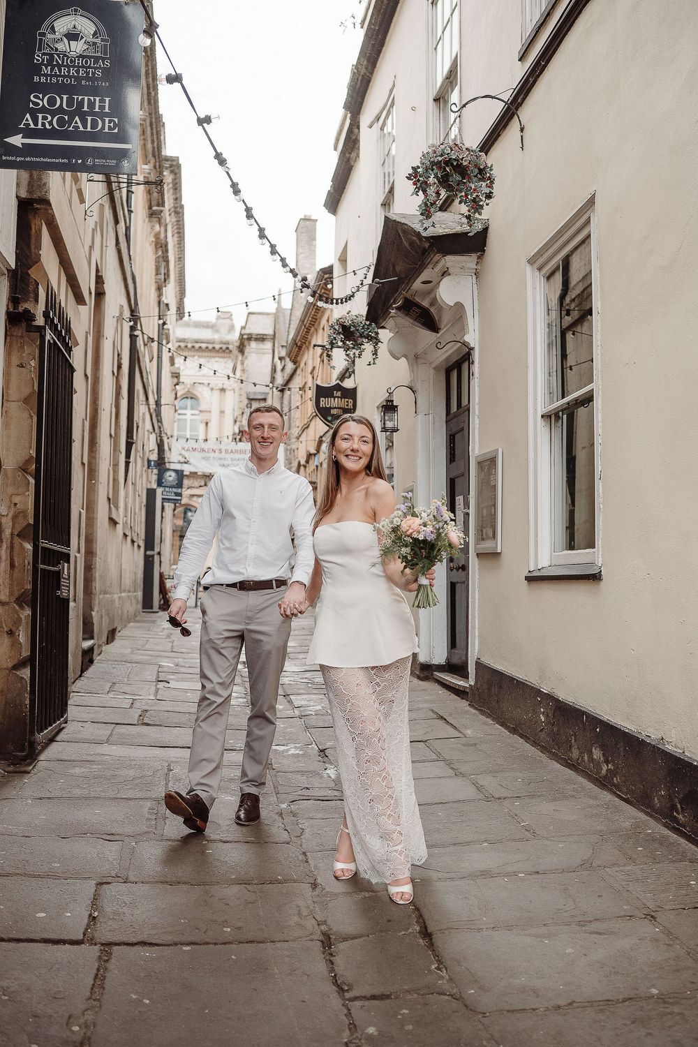 Bride and groom walking hand in hand through a charming cobblestone alley in Bath, England.