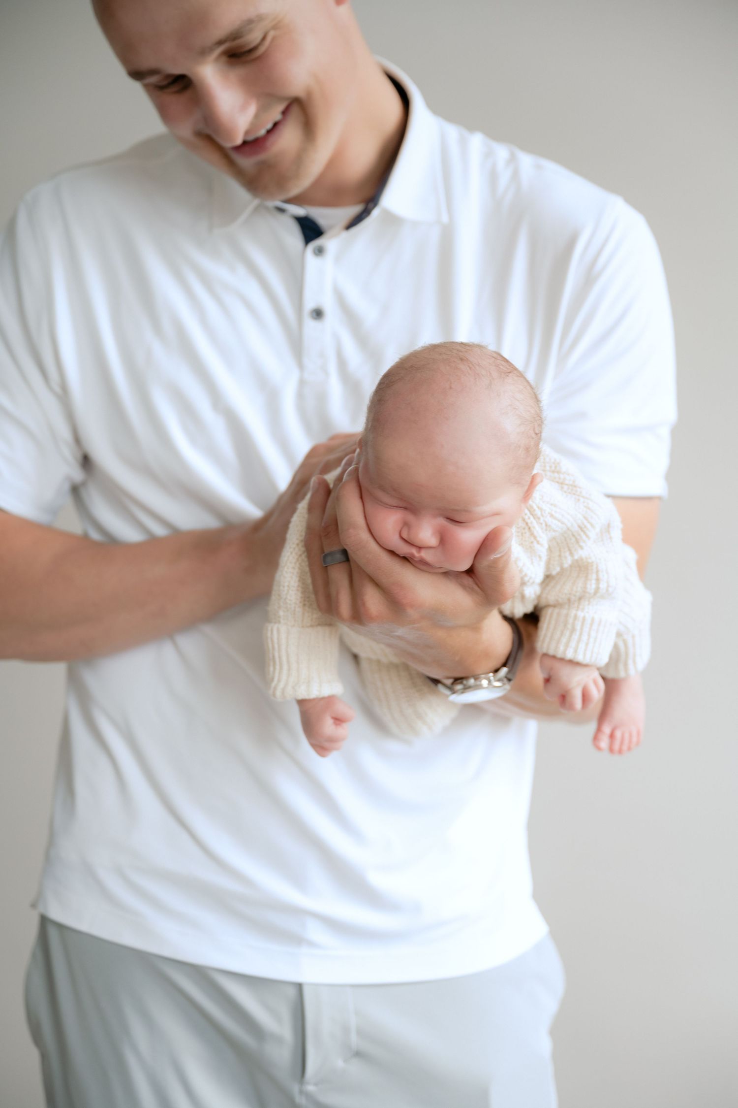 dad holding baby face on their stomach in his outstretched arm during in-studio lifestyle newborn session in stillwater, mn