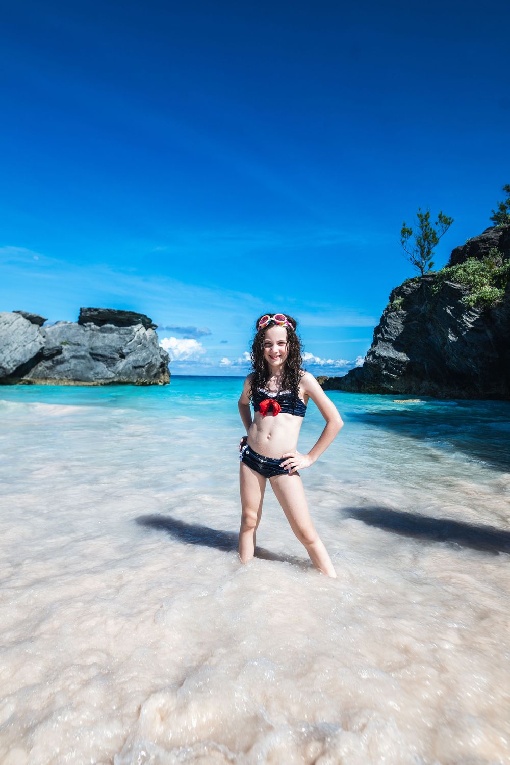 Young girl standing in crystal clear turquoise water at a scenic beach with rocky cliffs and blue sky. Horshoe Bay Beach