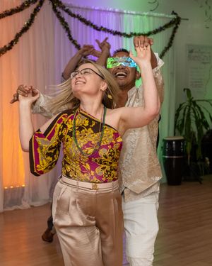 Two people dancing joyfully at a festive party, woman in colorful top and man wearing LED glasses.