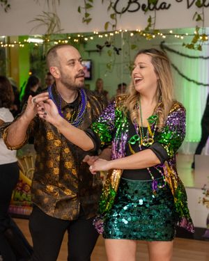 Couple dancing in Mardi Gras attire with colorful beads and sequin outfits at a festive indoor celebration.