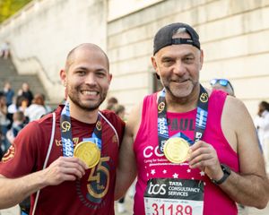 Two marathon finalists proudly display gold medals at the London Marathon, wearing TCS race bibs.