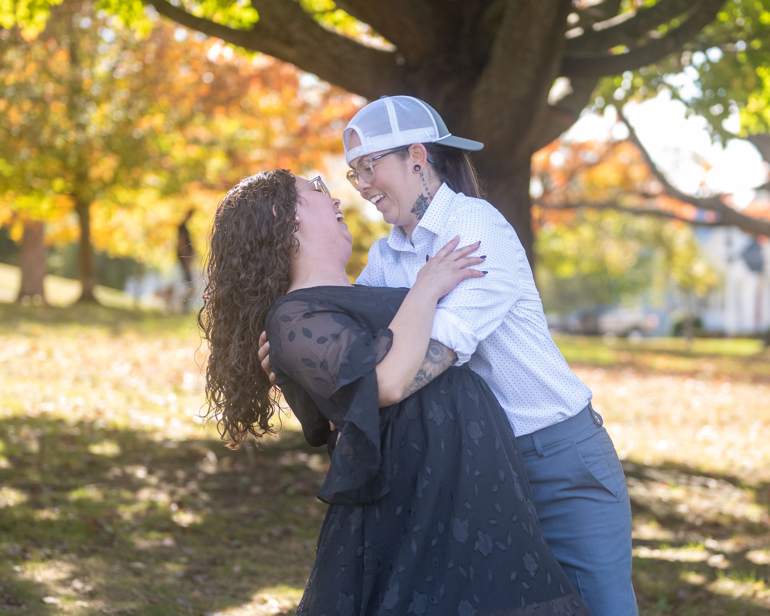 Couple dancing and laughing together outdoors under a colorful autumn tree in a park setting.