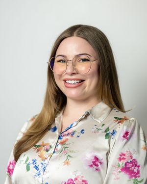 Smiling woman with glasses wearing a floral blouse against a light gray background.