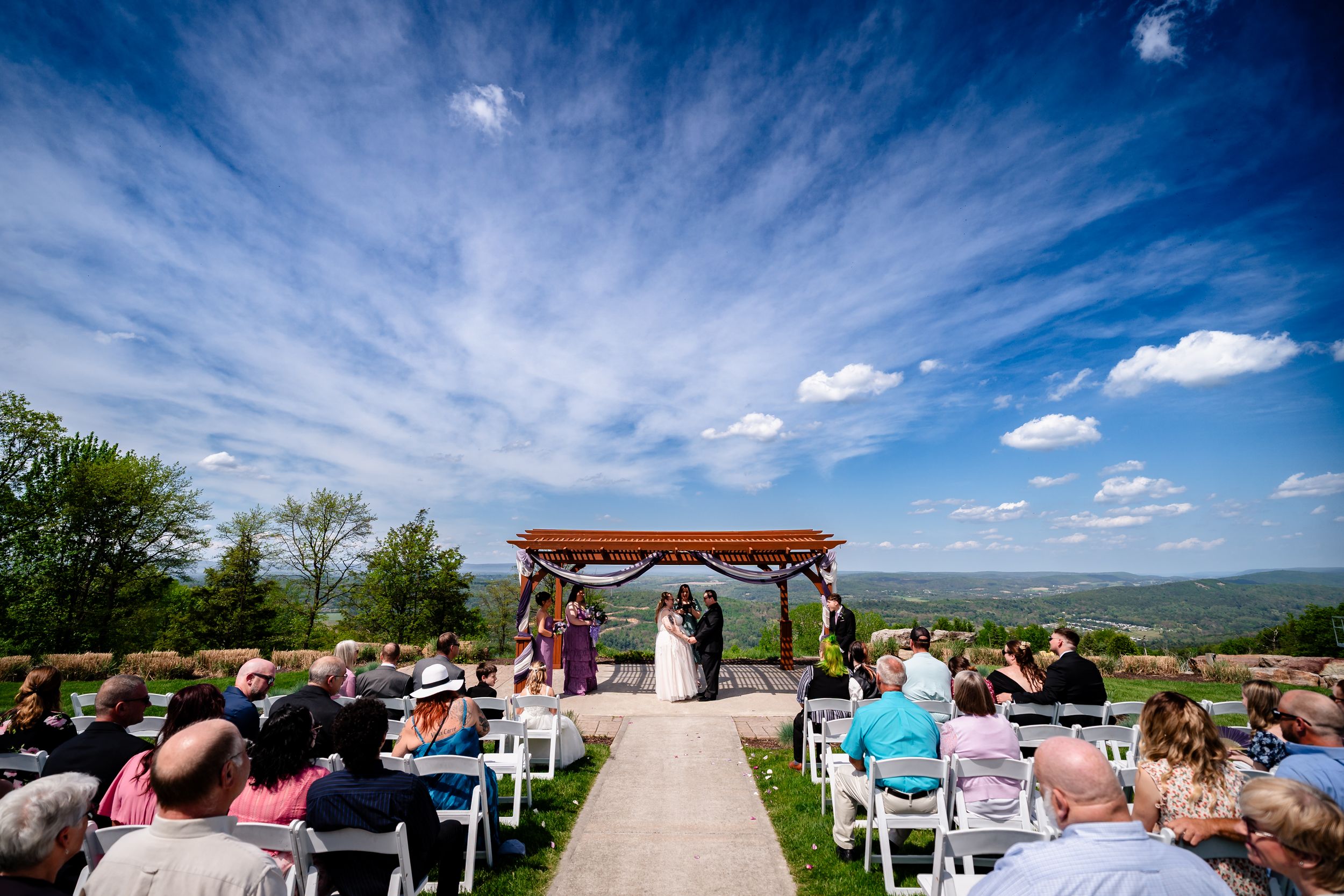 Outdoor wedding ceremony under pergola with stunning blue sky and sweeping valley landscape views.