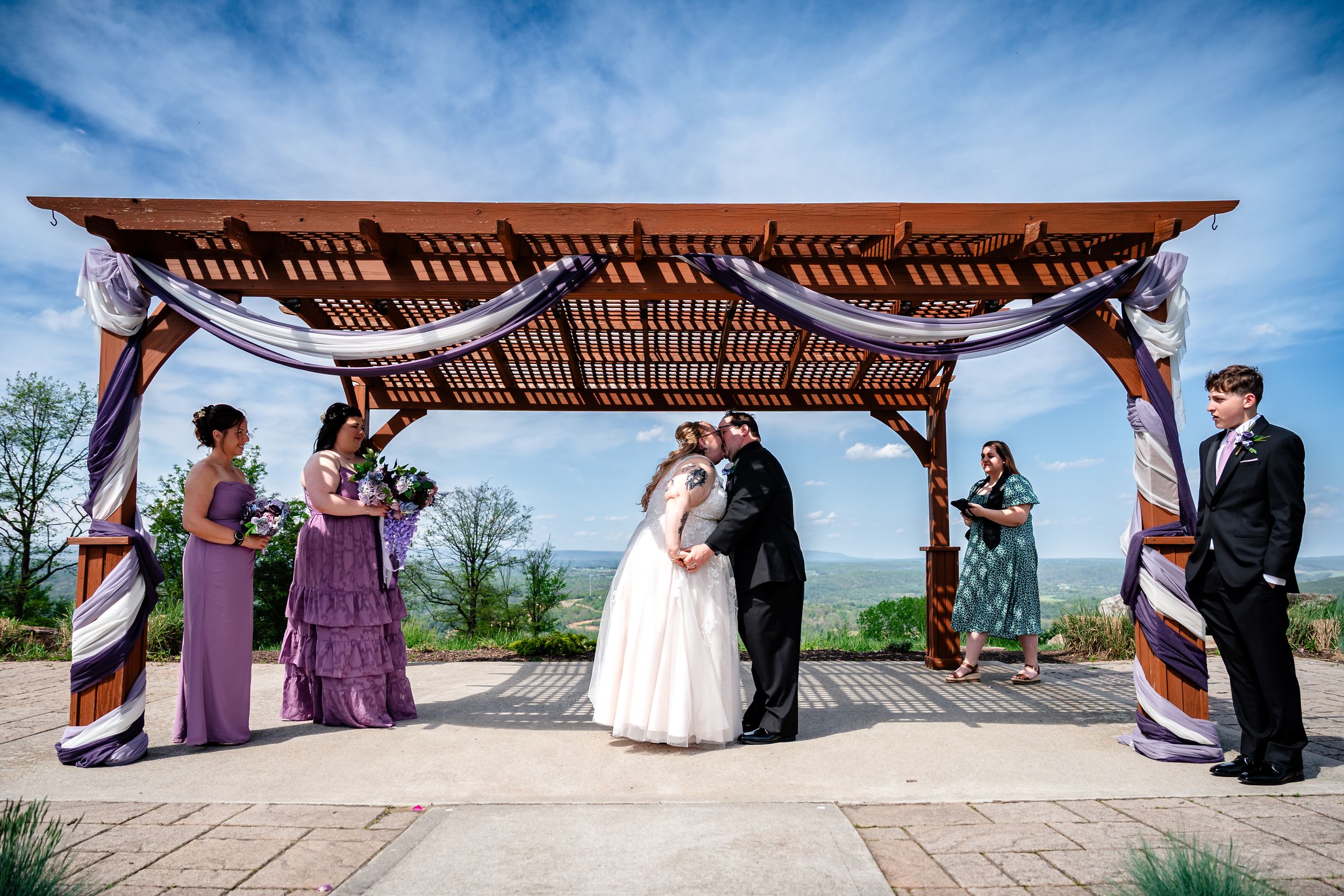 Wedding ceremony under wooden pergola with purple draping and mountain views.