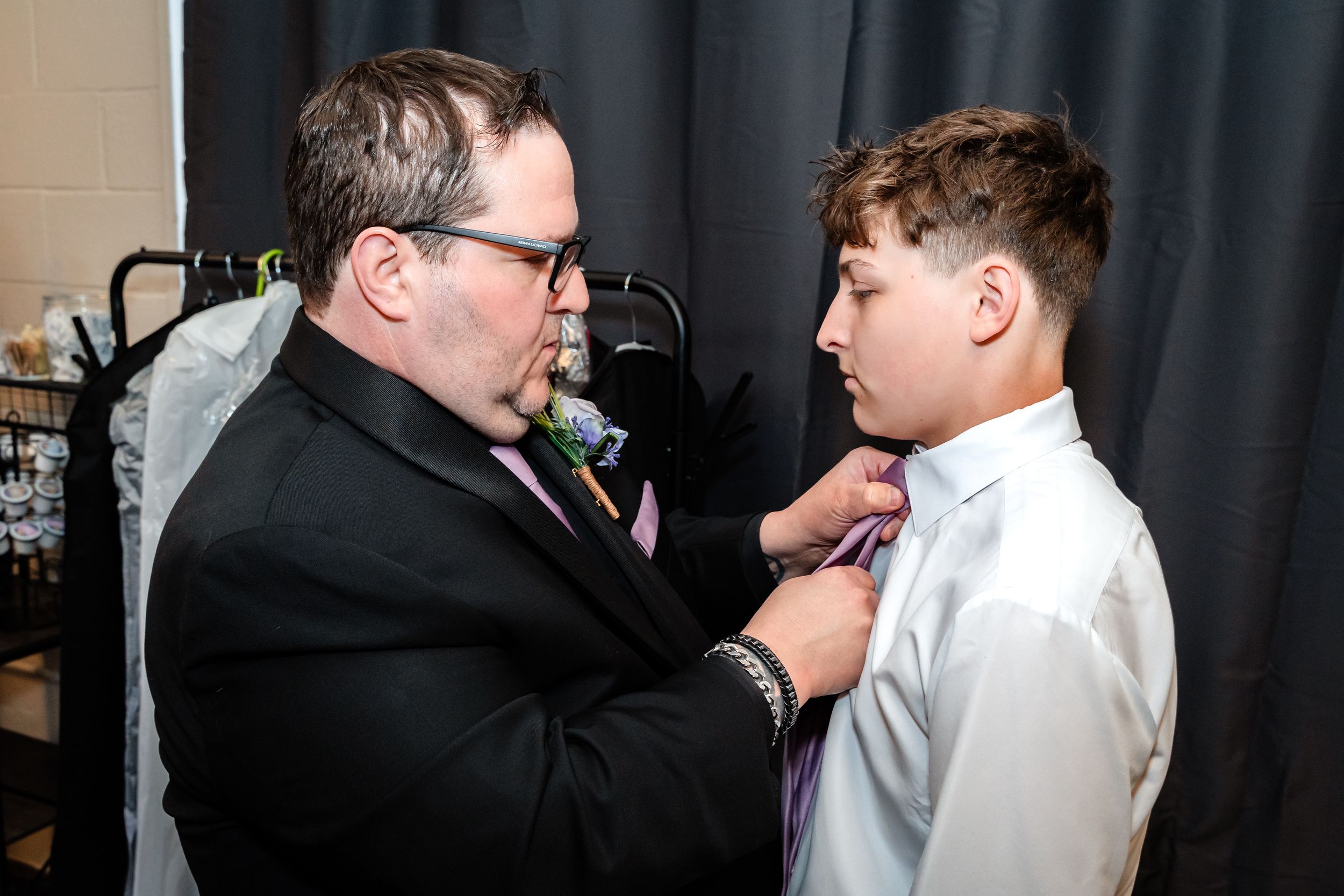 Man in black suit adjusting a boy's pink tie before a formal event.