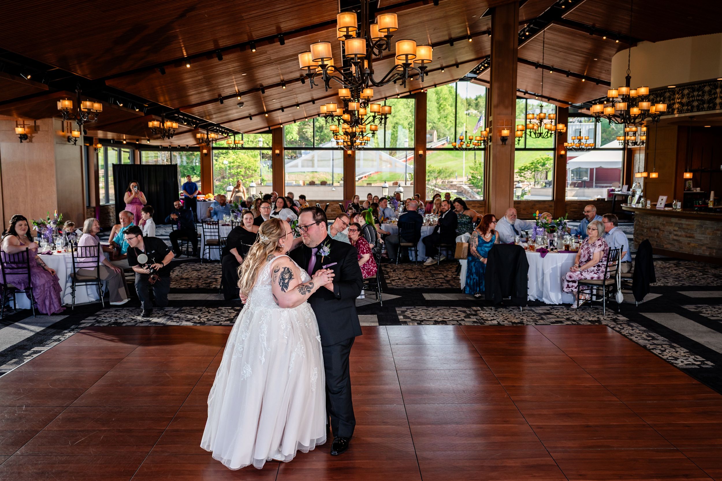 Bride and groom share first dance in elegant chandelier-lit wedding reception hall with guests.