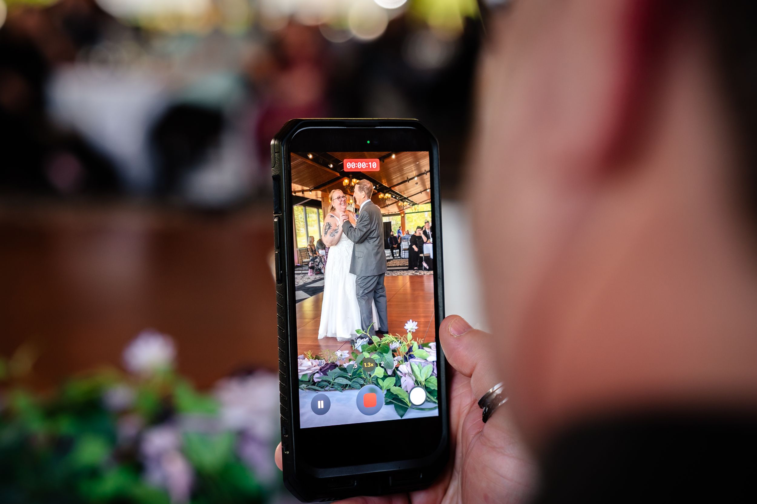 Wedding guest captures the newlyweds first dance on a smartphone during the indoor reception celebration.
