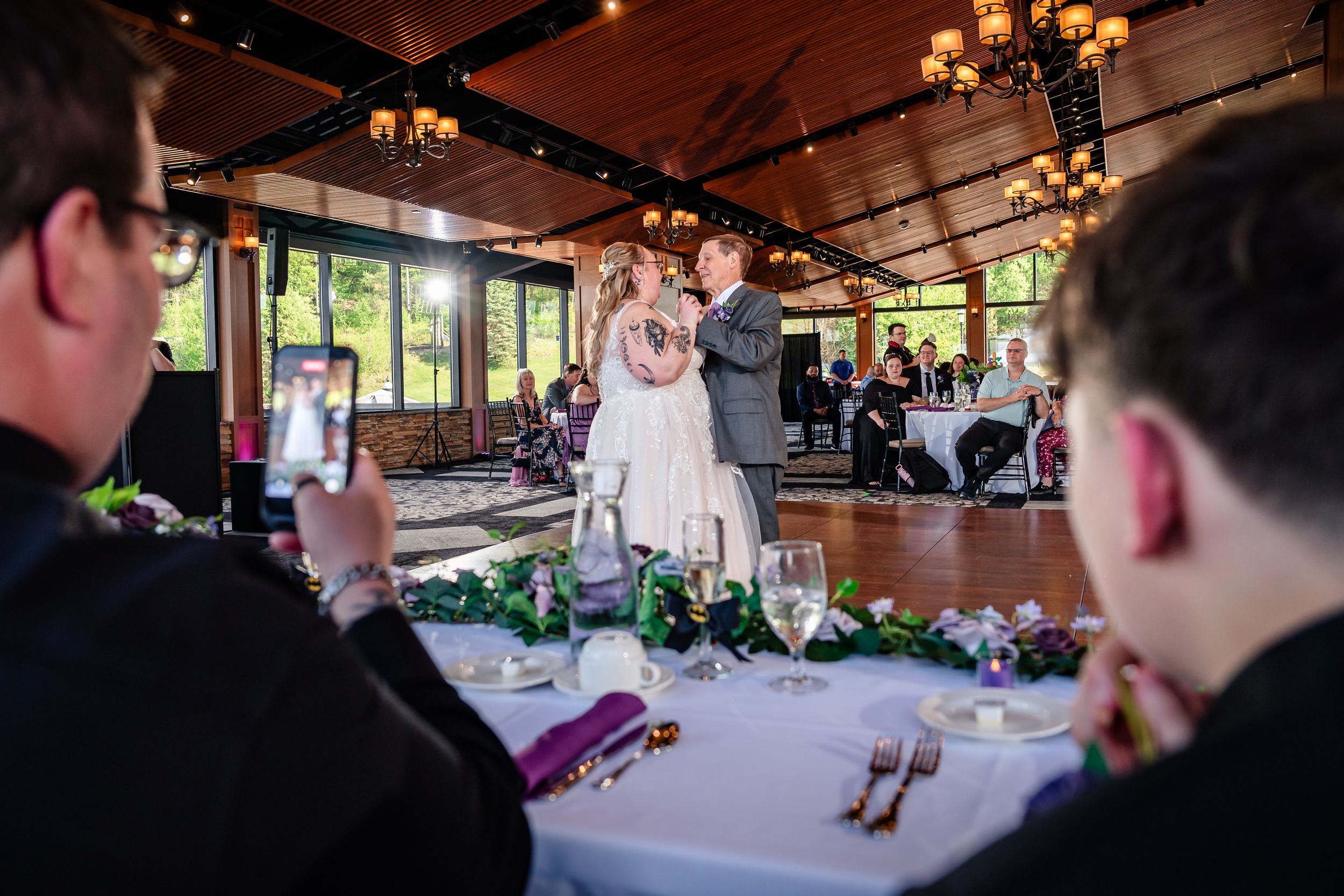 Guests watch bride and groom share first dance in warmly lit wedding reception venue.