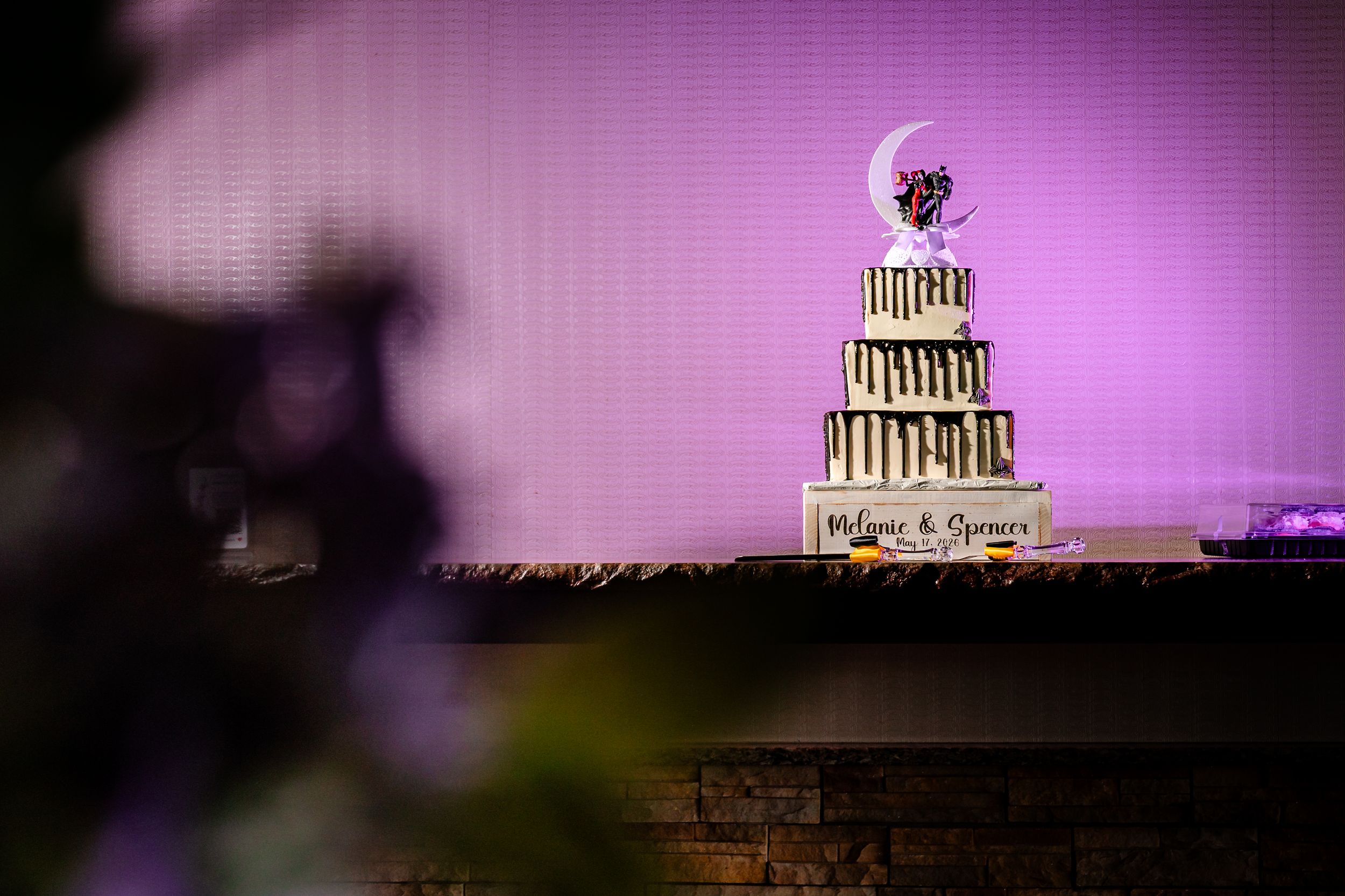 Elegant multi-tiered wedding cake with gold details displayed against a purple-lit backdrop at reception.