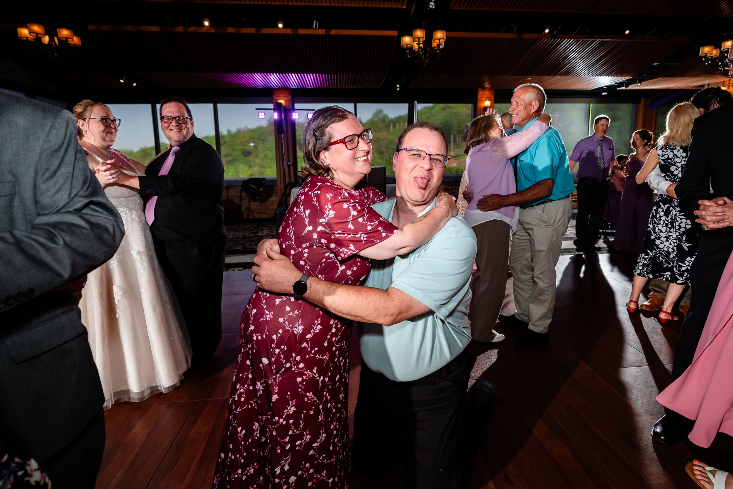 Couples dance together on crowded wedding reception dance floor in rustic venue with warm lighting.