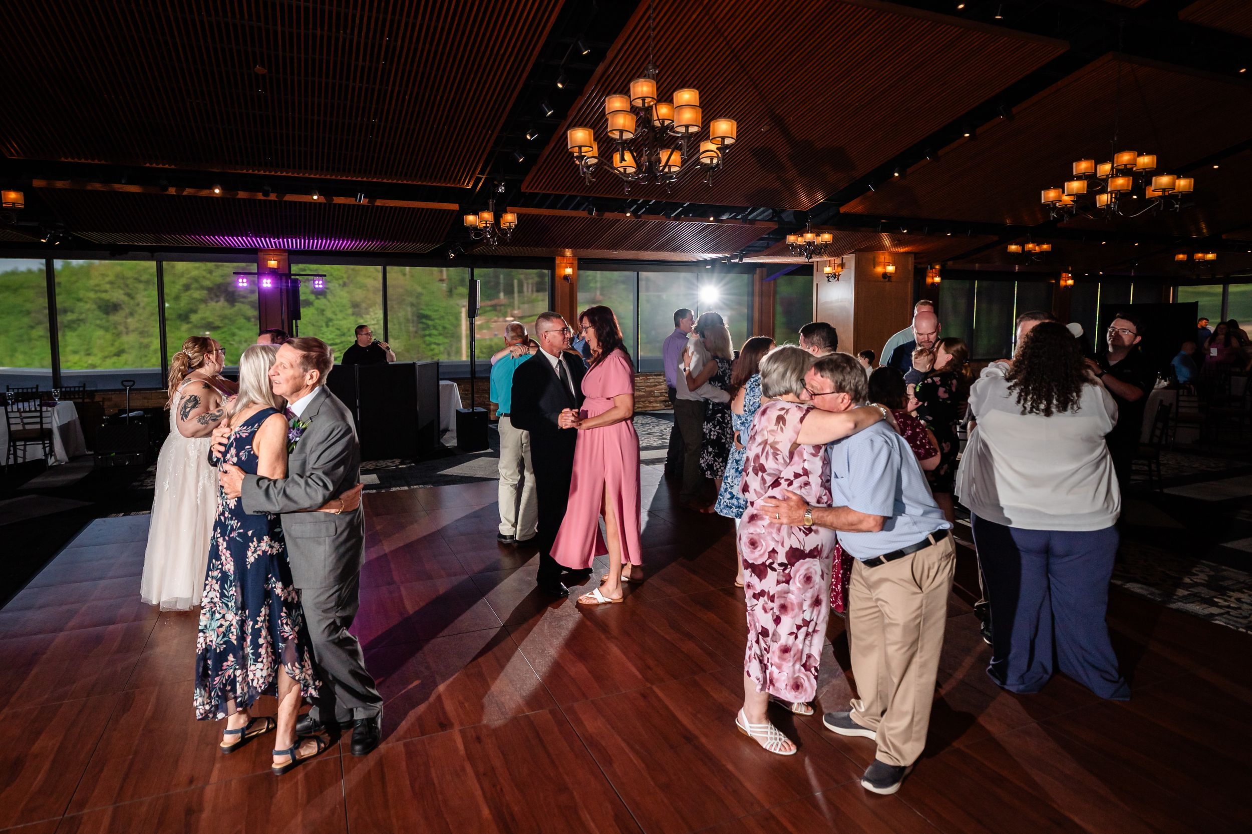 Wedding guests dancing together on a hardwood dance floor in an elegant reception venue with warm lighting.