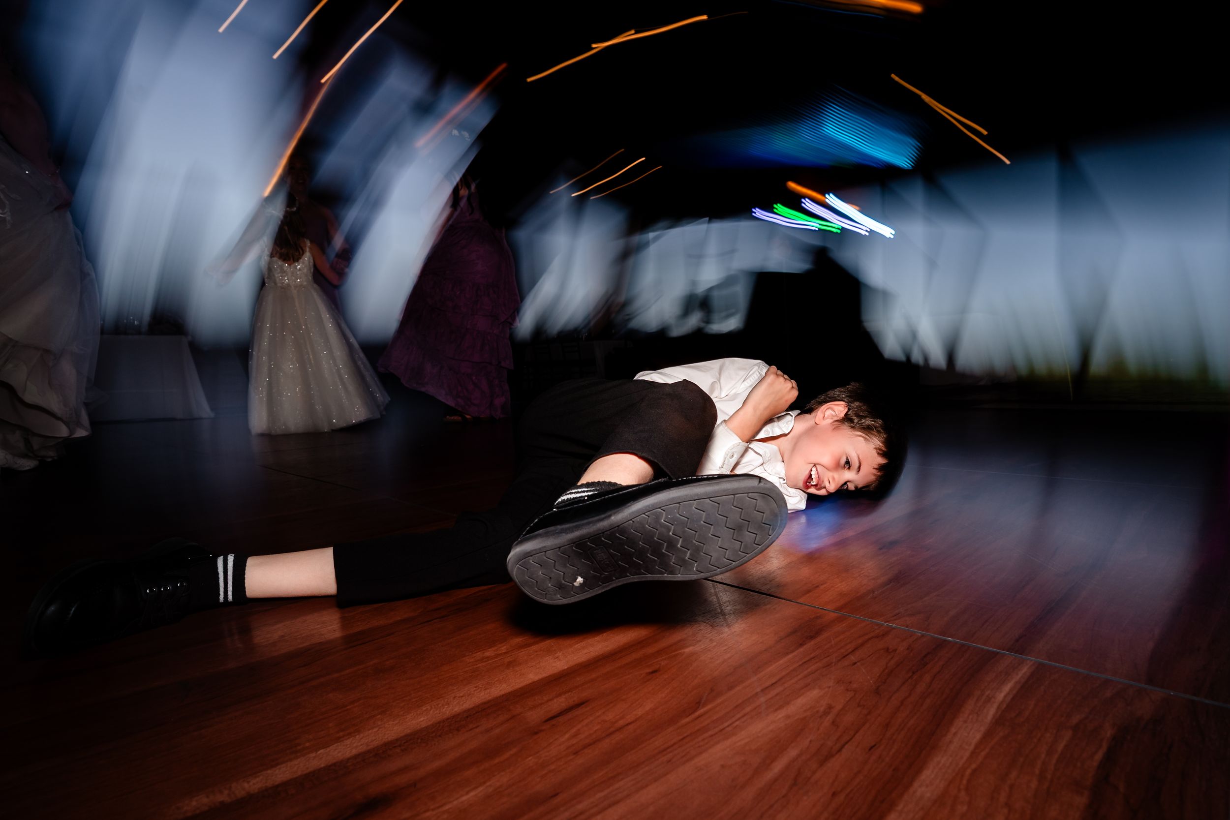 Person lying on a wooden dance floor with motion blur lights during a lively nighttime event.