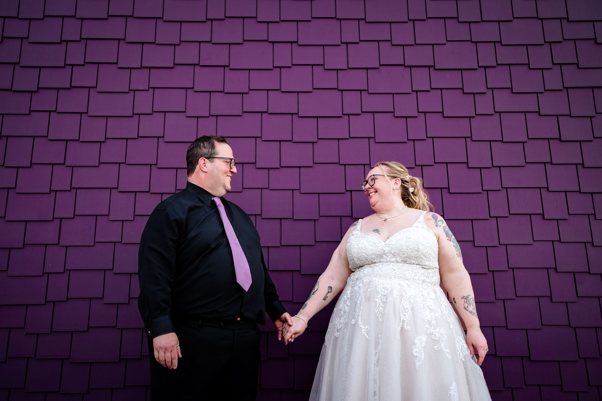 Bride and groom holding hands in front of purple textured wall portrait.