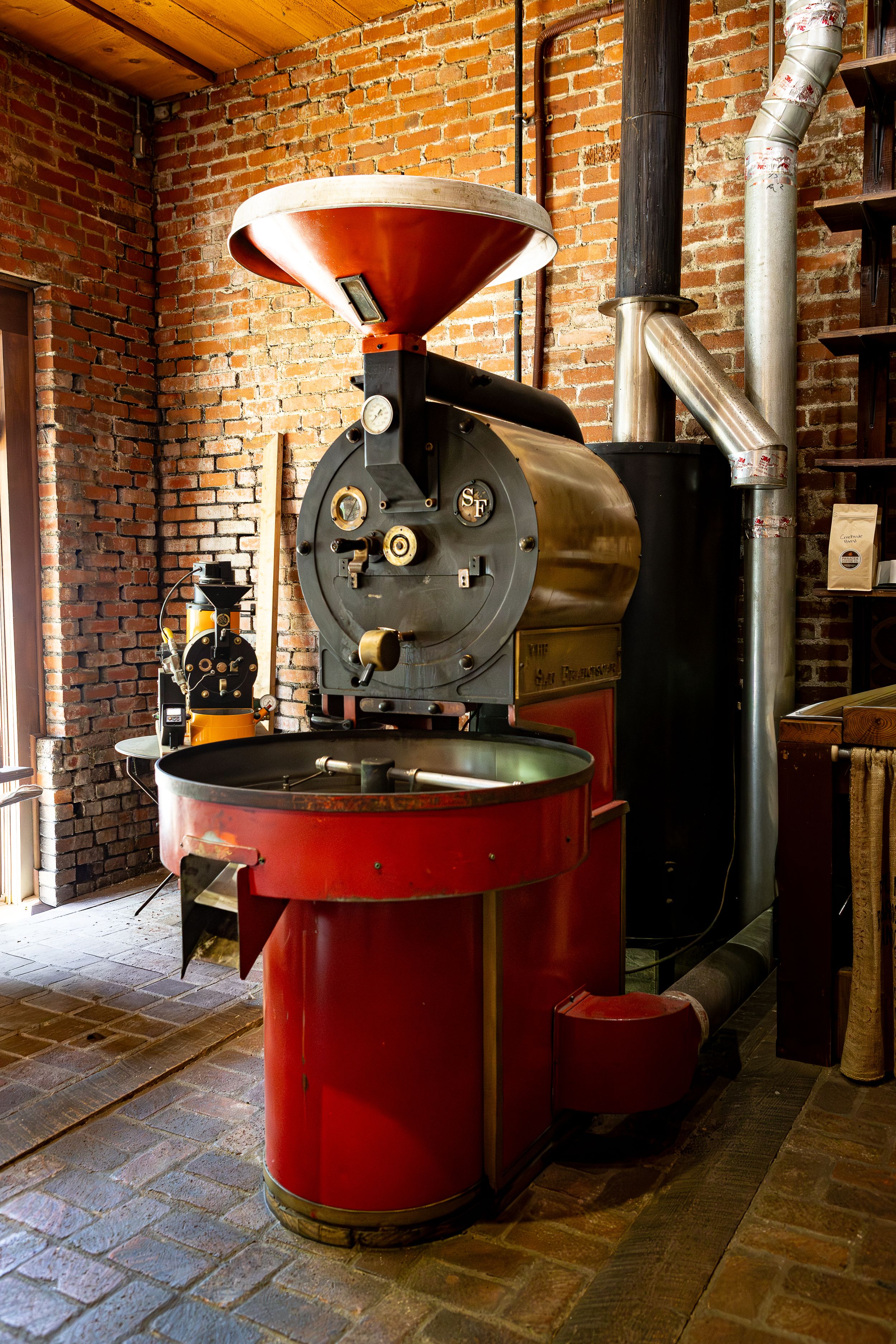 Vintage coffee roaster machine in a rustic brick-walled interior with metal pipes Brand photography in Waynesville NC coffee shop