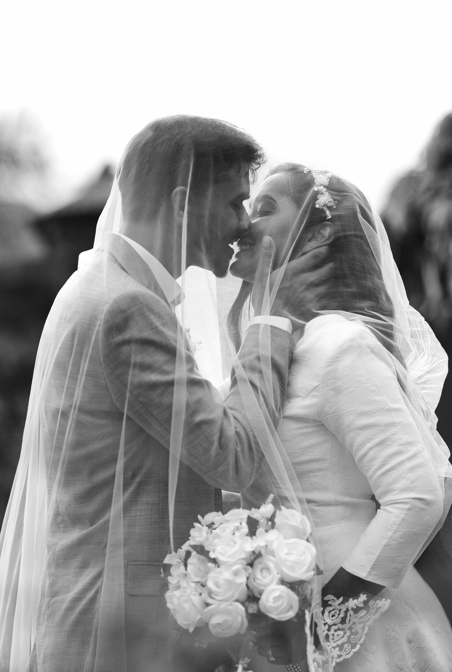 A romantic black and white wedding photo sequence showing a tender kiss between newlyweds through a delicate veil.