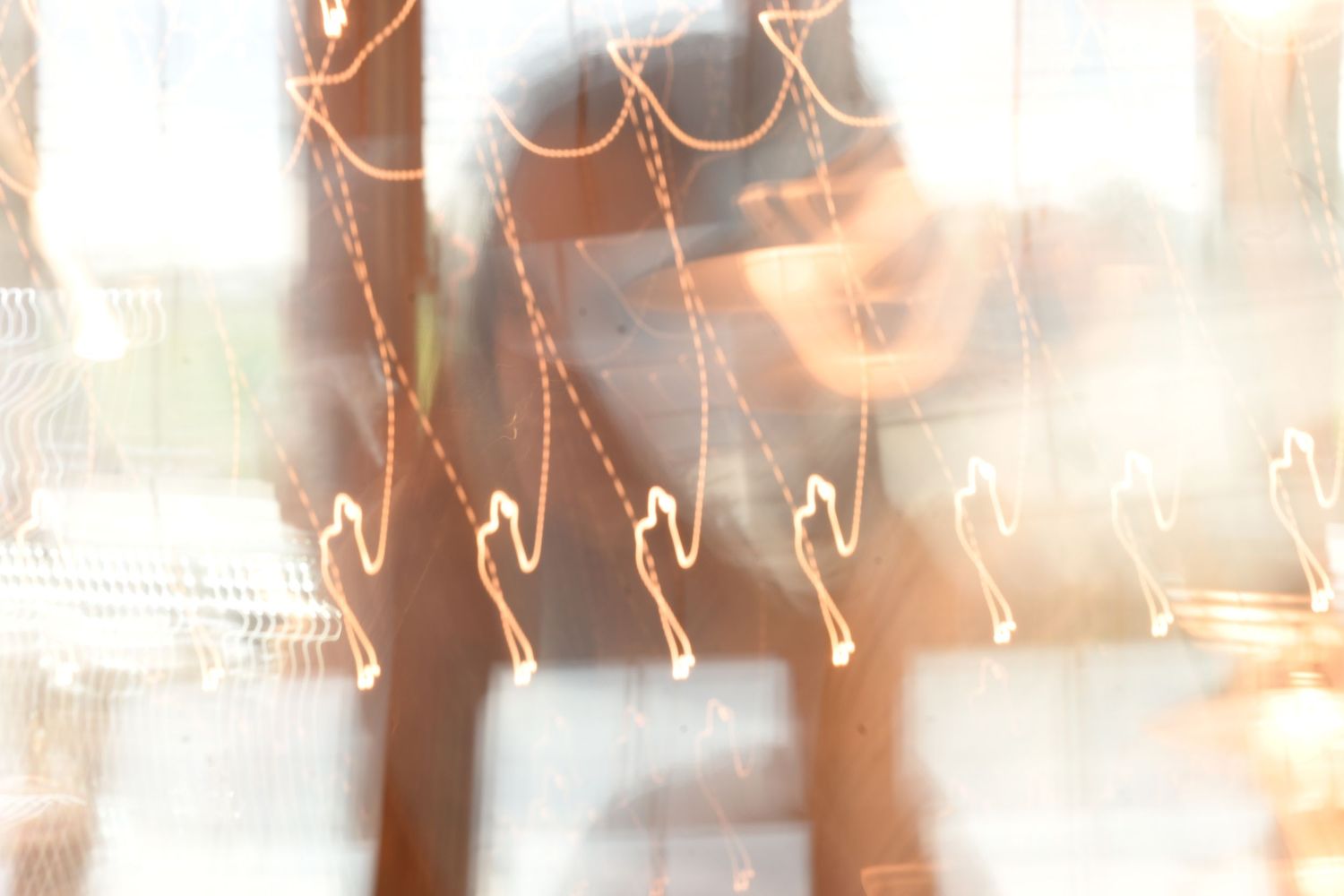Blurry abstract photo of a person behind glass with bokeh light trails creating a dreamy, artistic effect.