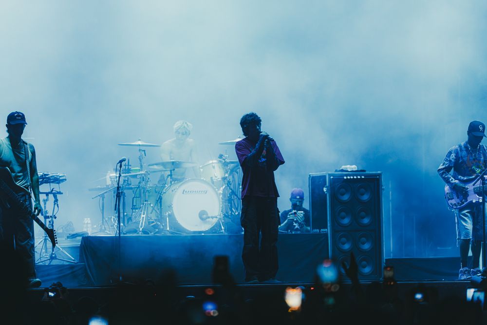 Band performing on a foggy stage with blue lighting, drummer and guitarist visible at a live concert.