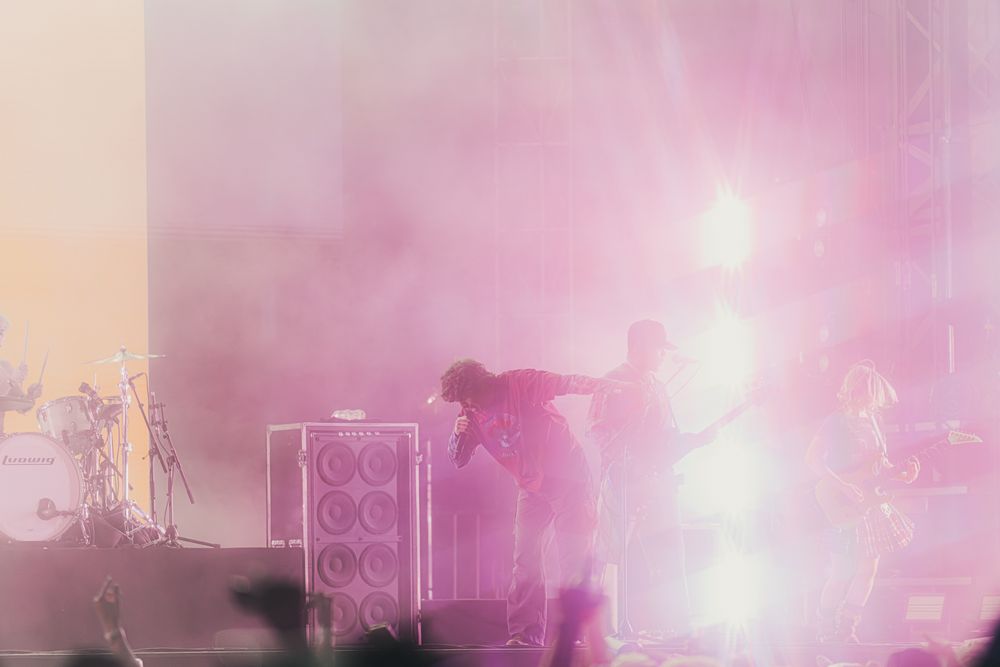 Silhouetted band performing on stage surrounded by pink and purple smoke with bright concert lights.