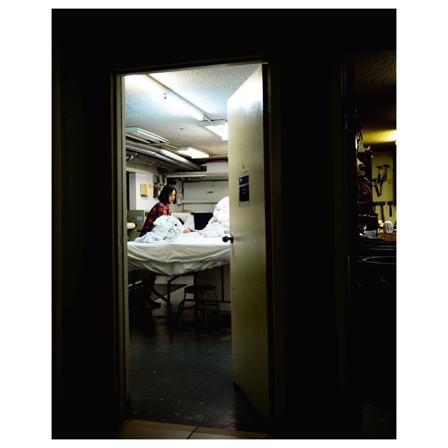 A person sits on a hospital bed viewed through a dimly lit doorway in a dark room.