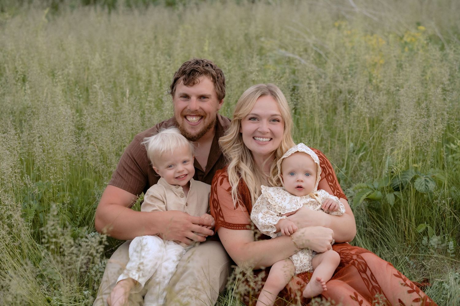 family sitting in tall summer grasses during outdoor lifestyle family session in somerset wisconsin