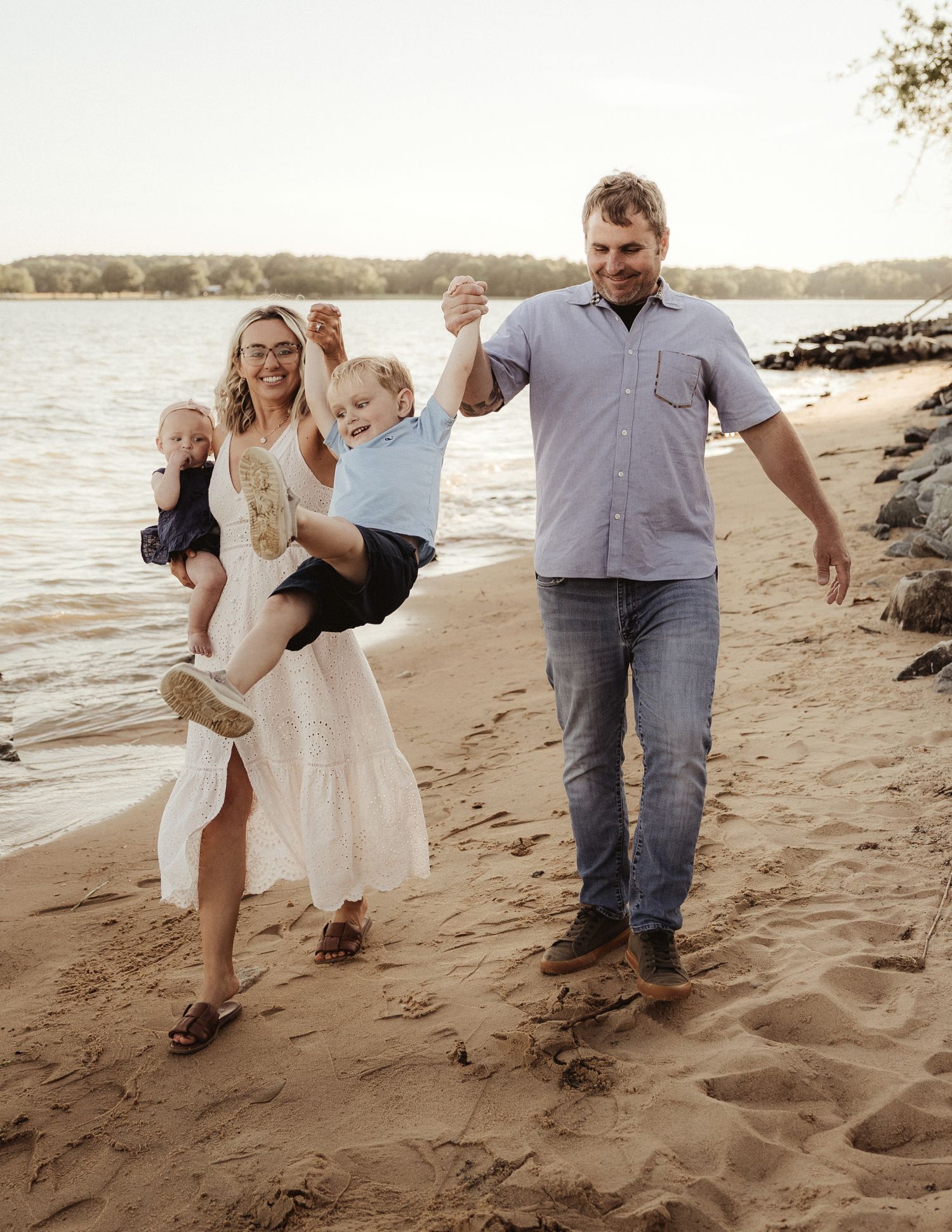 Happy family of four playing on a sandy beach, parents swinging children while walking along the shoreline.