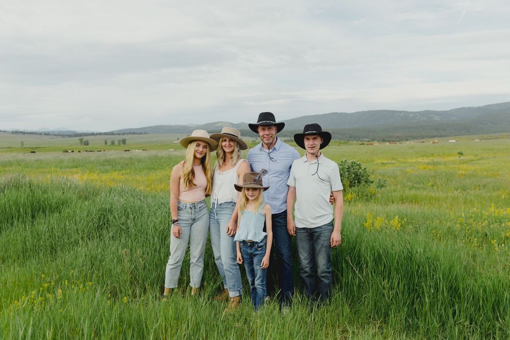 Family of five in cowboy hats posing in a lush green meadow with wildflowers and rolling hills.