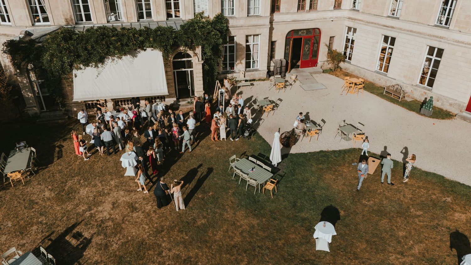 Aerial view of elegant outdoor wedding reception gathering in a historic chateau courtyard with lush greenery.