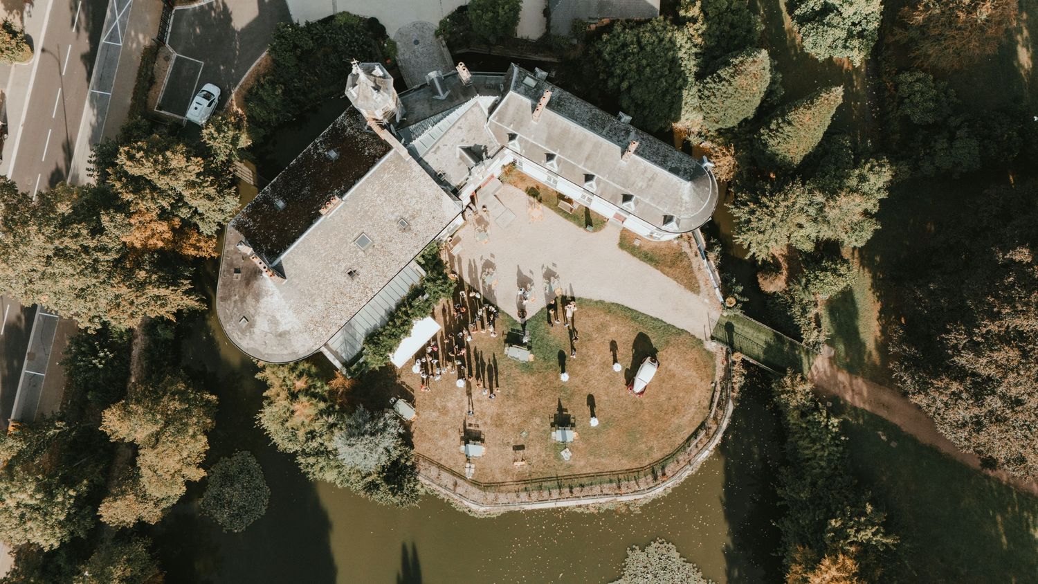 Aerial drone view of a historic castle surrounded by water and lush trees in autumn.
