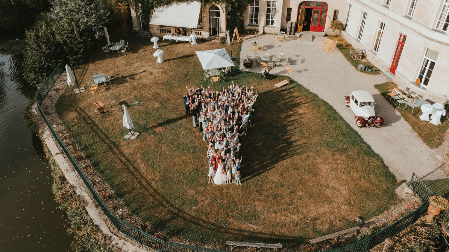 Aerial view of wedding guests gathered on a green island surrounded by water near a French château.