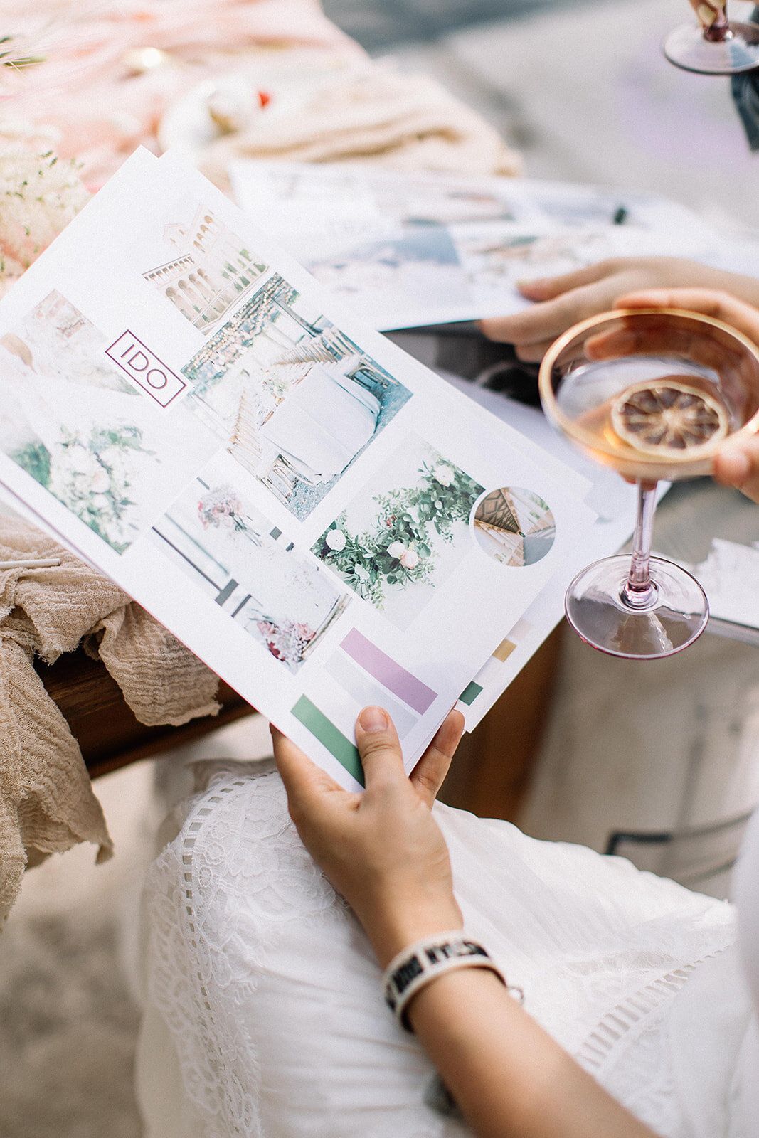 Bride holding open wedding planning magazine with mood board while holding a glass of rose wine.