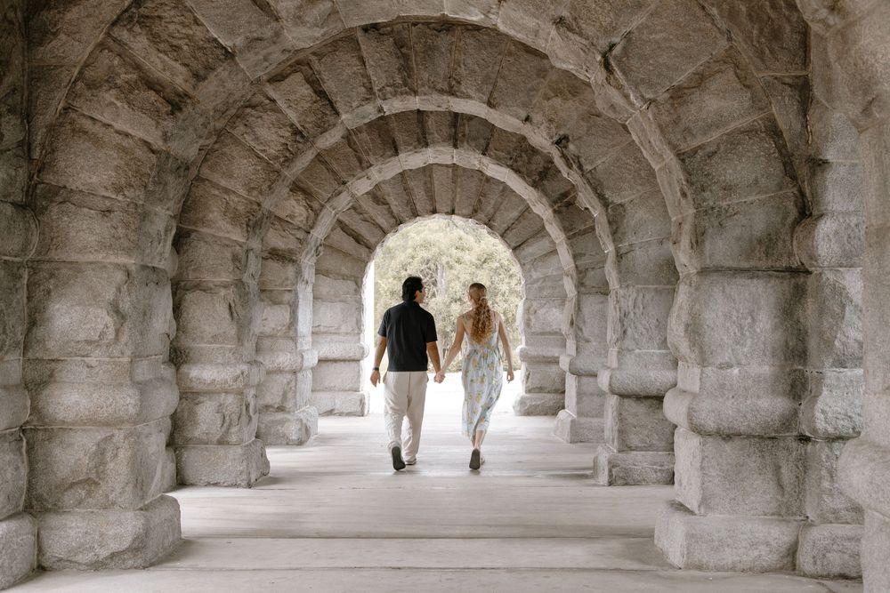 Couple holding hands walking through ancient stone archway tunnel at historic ruins.