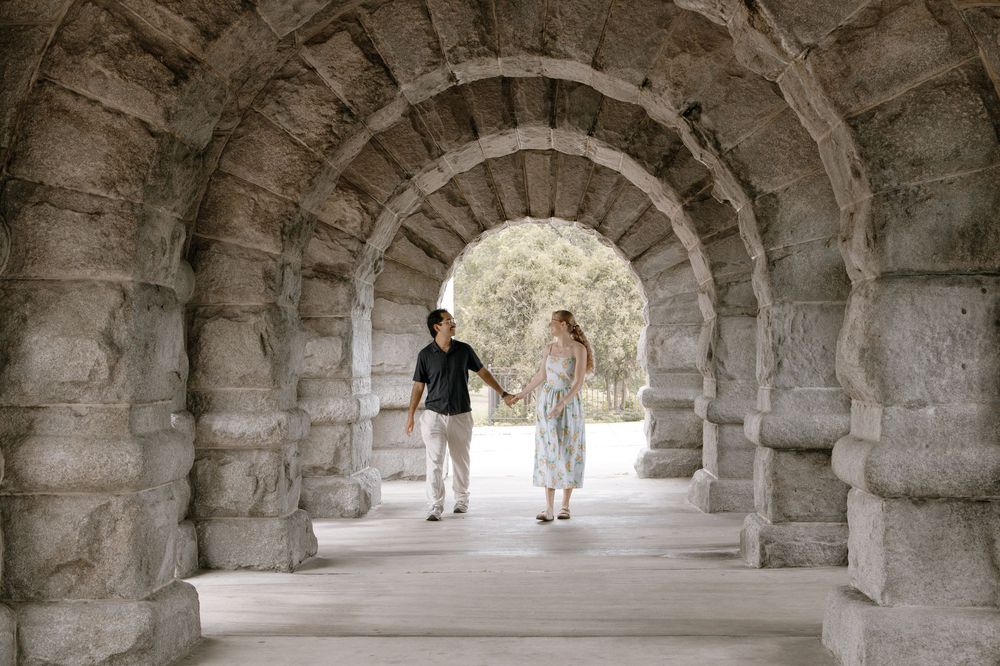 Couple holding hands walking through stone archway tunnel in a romantic outdoor setting.