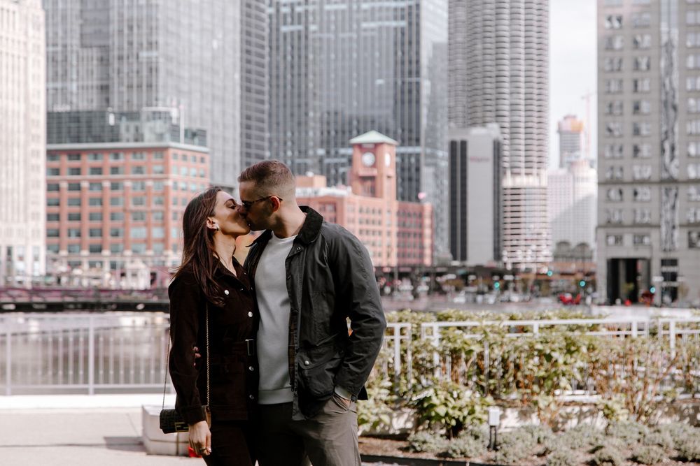 Couple kissing on a riverside terrace with Chicago city skyline skyscrapers in the background on a sunny day.