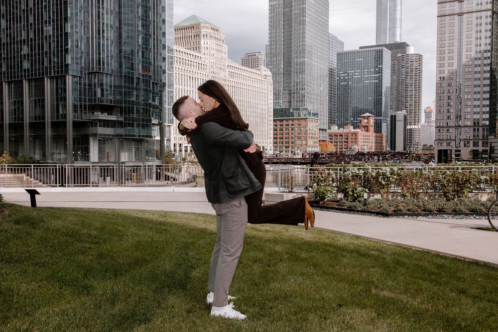Couple embracing and spinning in front of Chicago city skyline on a green lawn during an outdoor engagement photo session.