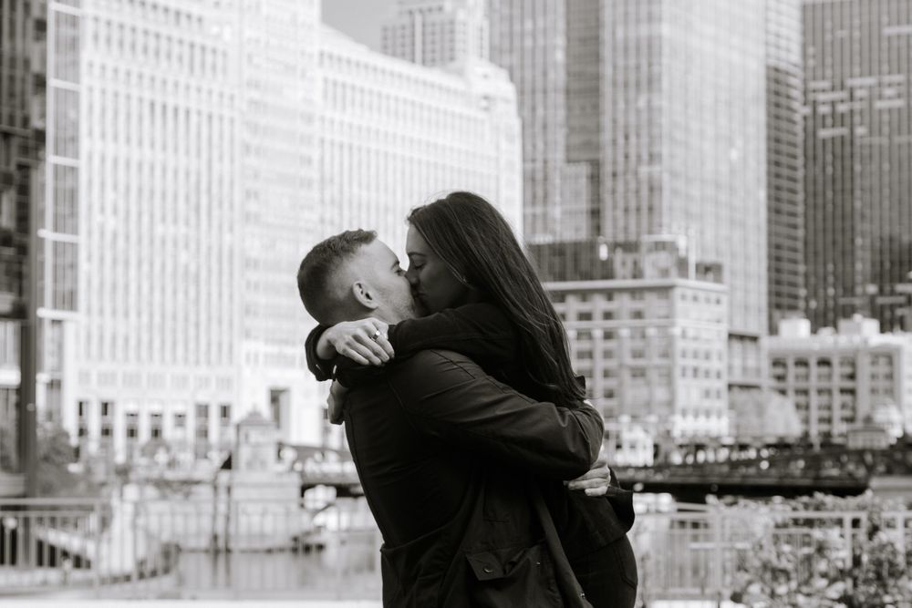 A couple shares a romantic kiss against a stunning black and white cityscape backdrop in an urban engagement photo.