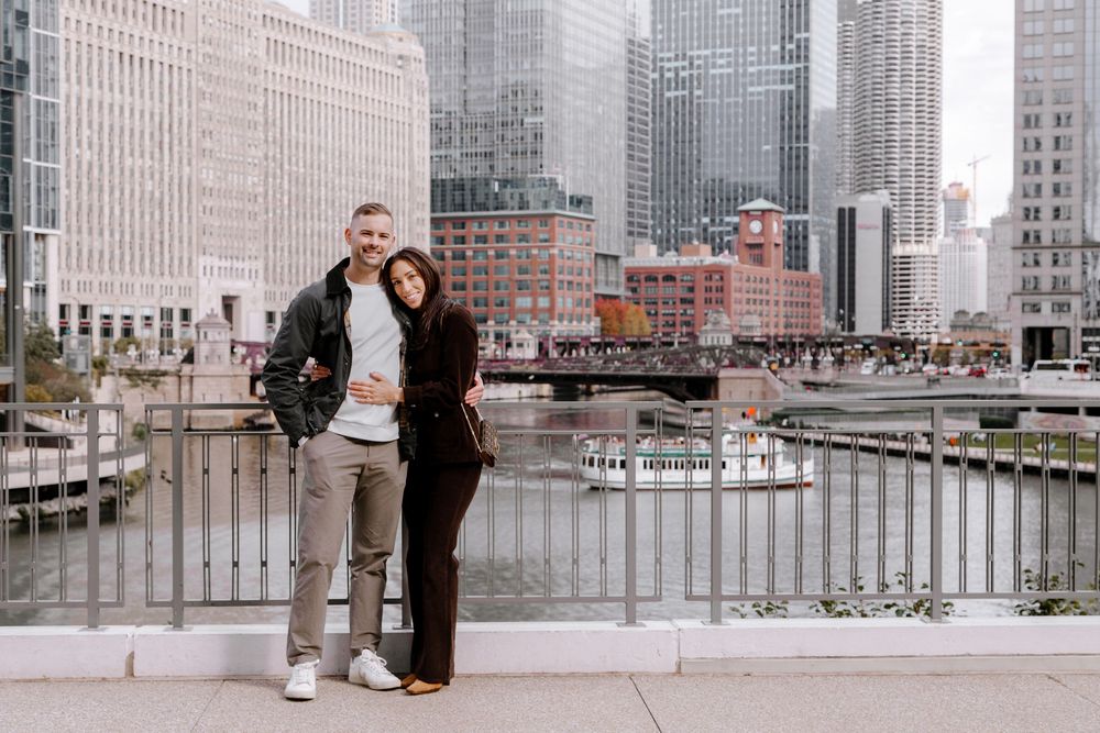 Couple posing together on a city bridge with Chicago River and skyscrapers in the background.