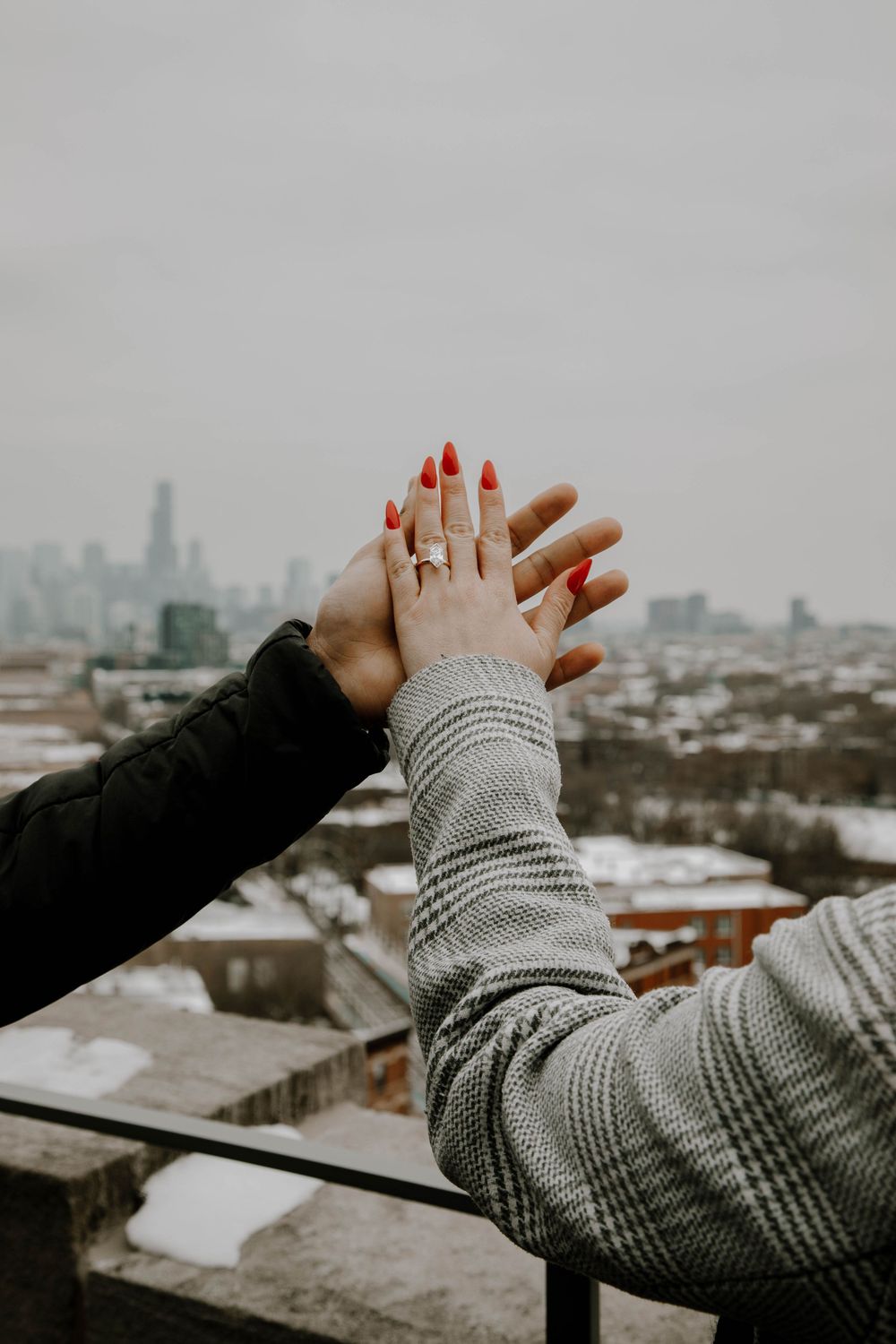 Close-up of couple holding hands showing engagement ring with city skyline in background.