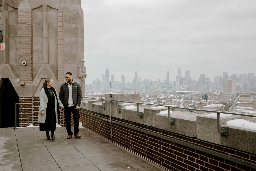 Couple standing on a rooftop terrace with the Chicago city skyline visible in the misty background.