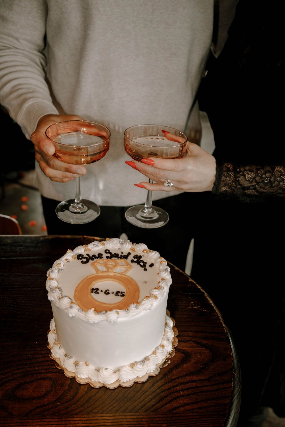 Couple toasts champagne over white engagement cake reading She Said Yes with date 12.6.23.