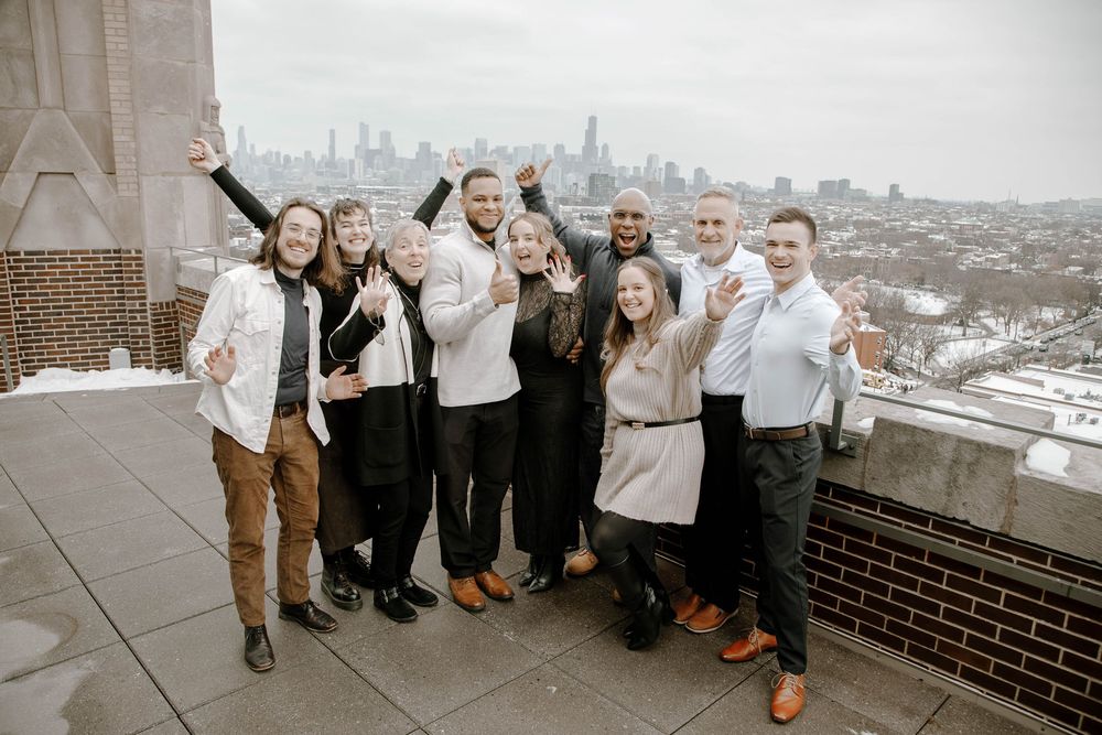 Group of people posing and celebrating on a rooftop with a city skyline in the background on a winter day.