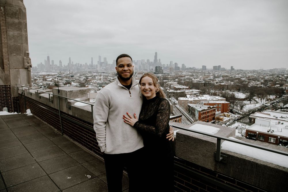 Couple smiling together on a rooftop with Chicago city skyline in the background on a cloudy winter day.