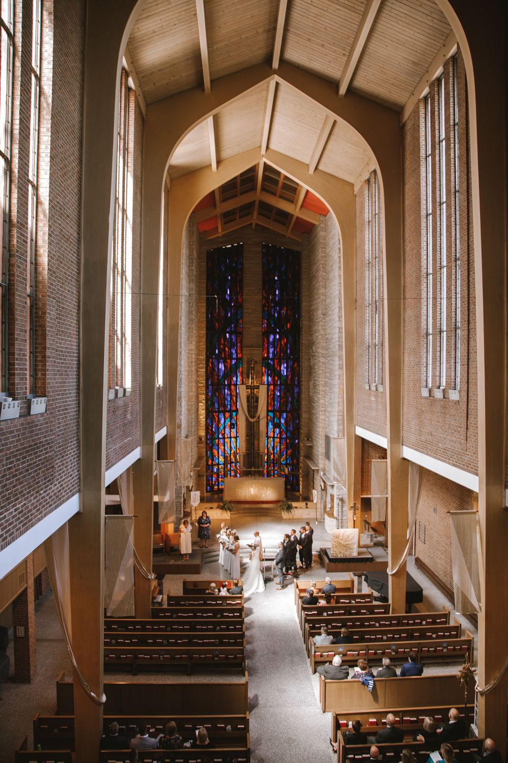 Aerial view of a church wedding ceremony with stained glass windows, wooden pews, and an arched ceiling.