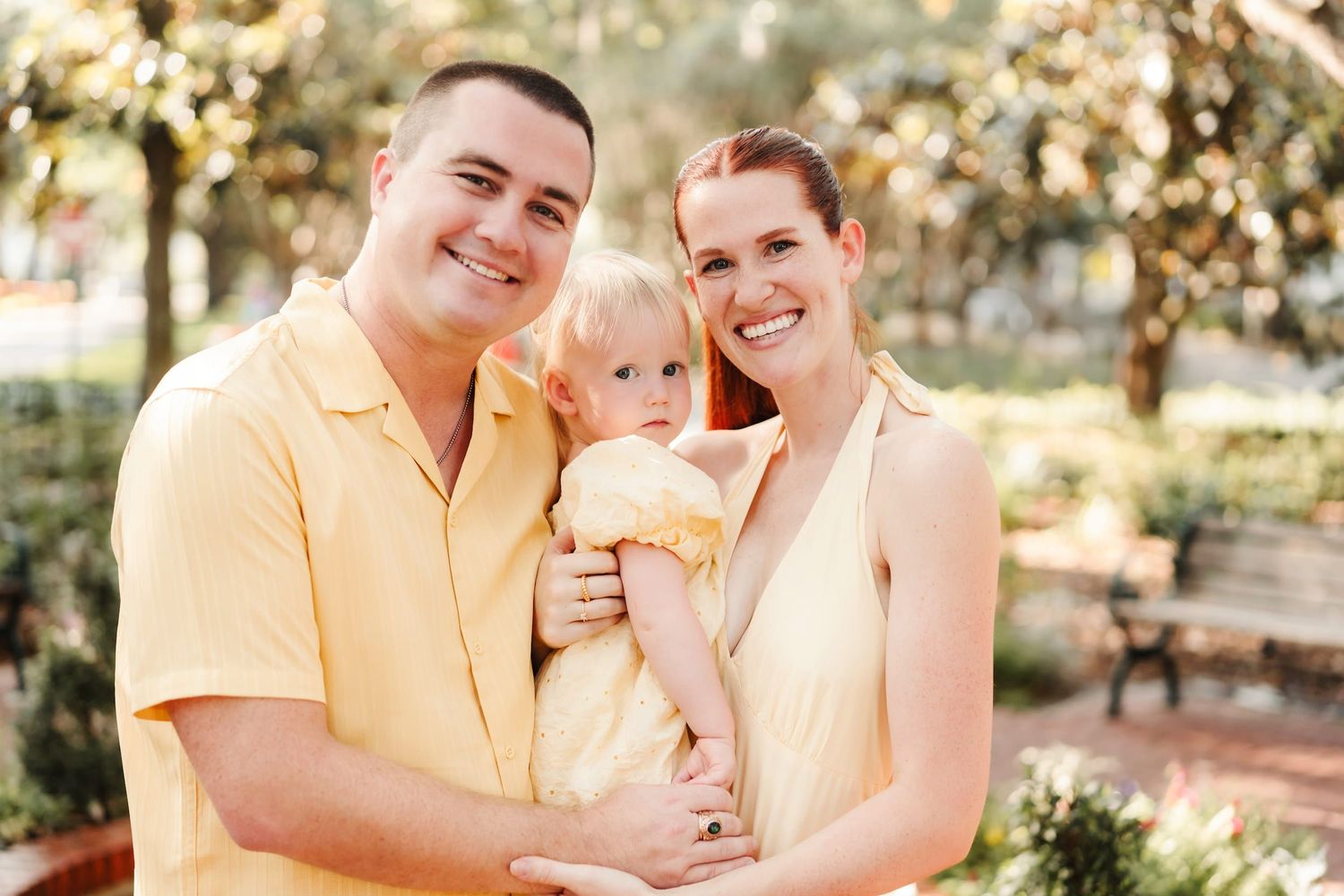 Three people in blue outfits sit together outdoors on a bench during golden hour lighting in a park setting.