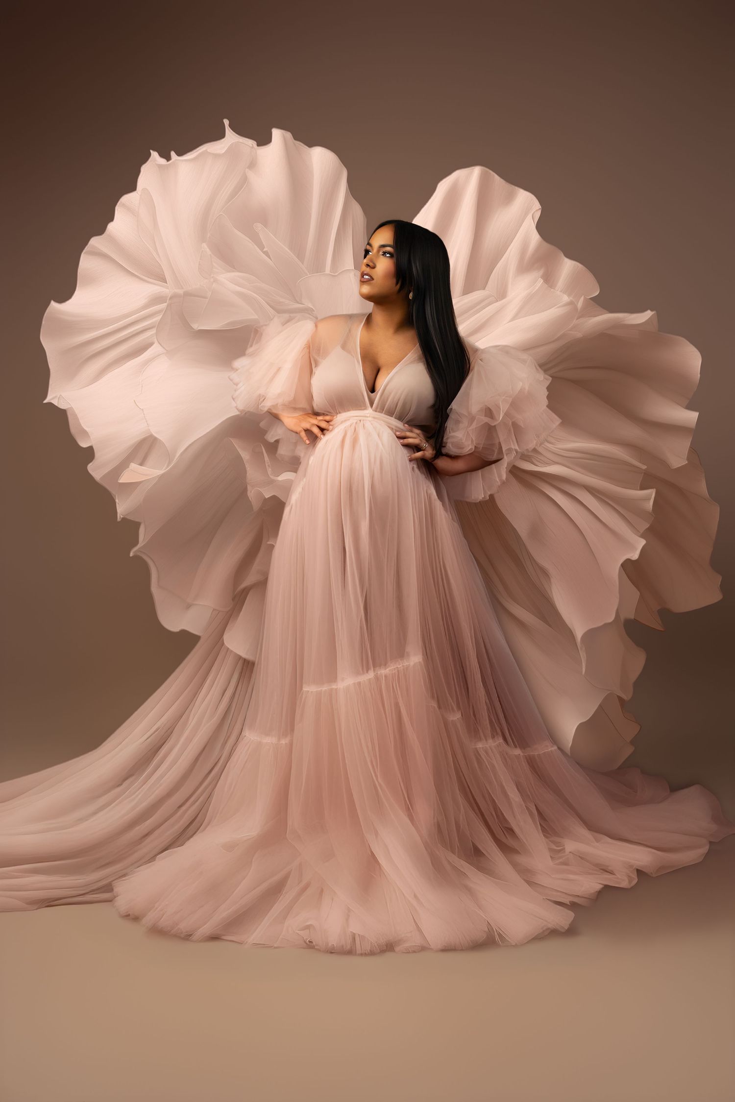 Pregnant woman in flowing pink tulle gown with dramatic billowing fabric wings.
